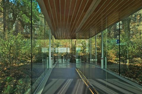 The sloping corridor between the public and private rooms is lined with mirror-polished steel, reflecting the woodland outside.