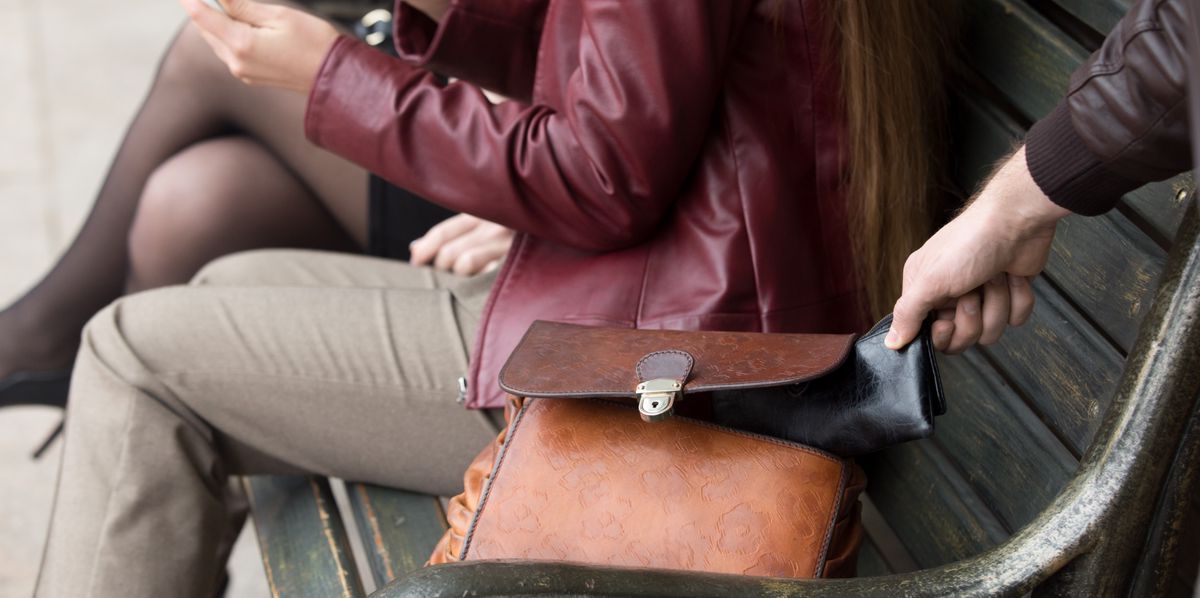 Street thief stealing a wallet from woman bag. Focus on theft hand. Close-up